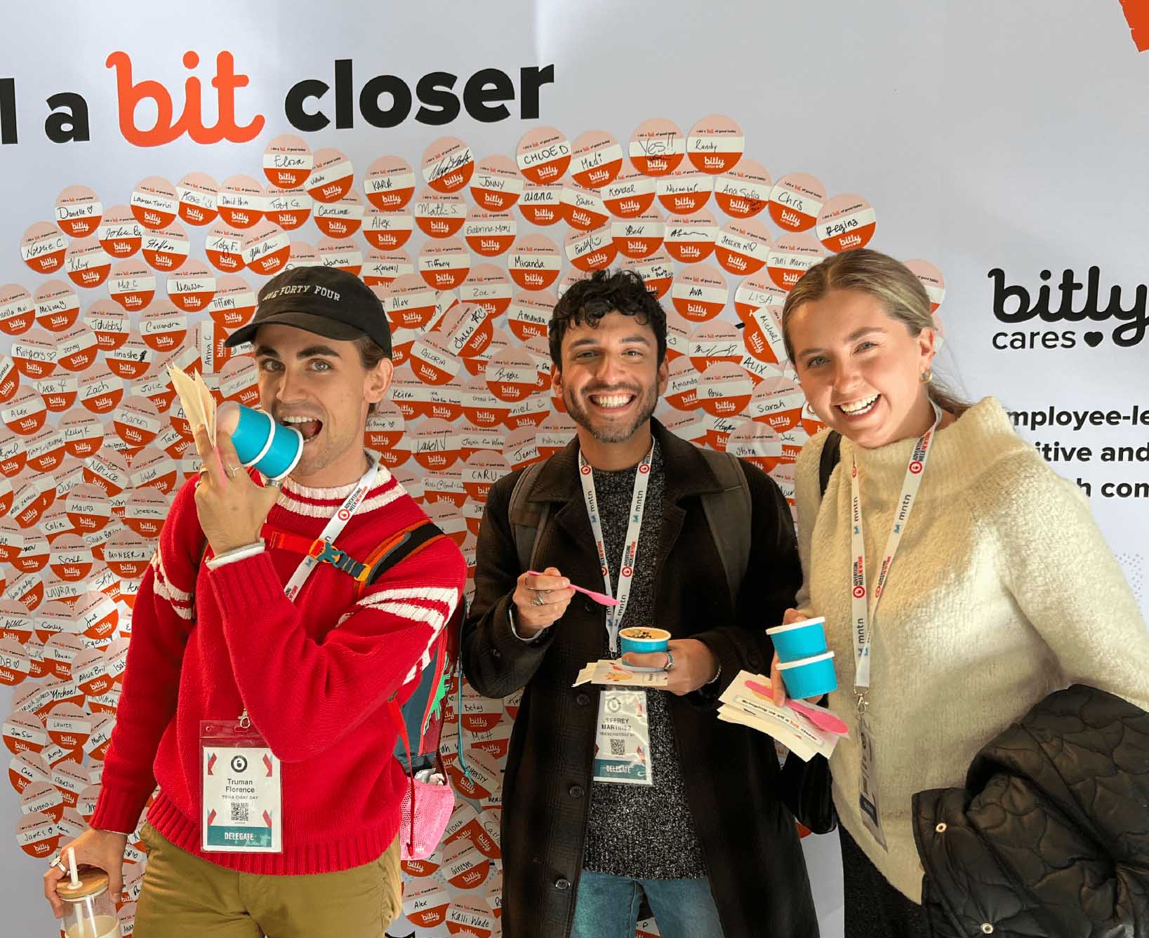 Three smiling people holding ice cream in front of a wall of stickers.