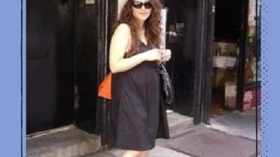 A woman standing outside in a black dress and sunglasses.