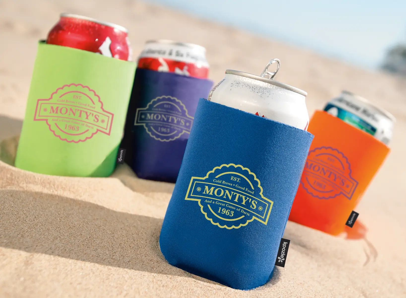 Four cans in Koozies in the sand.