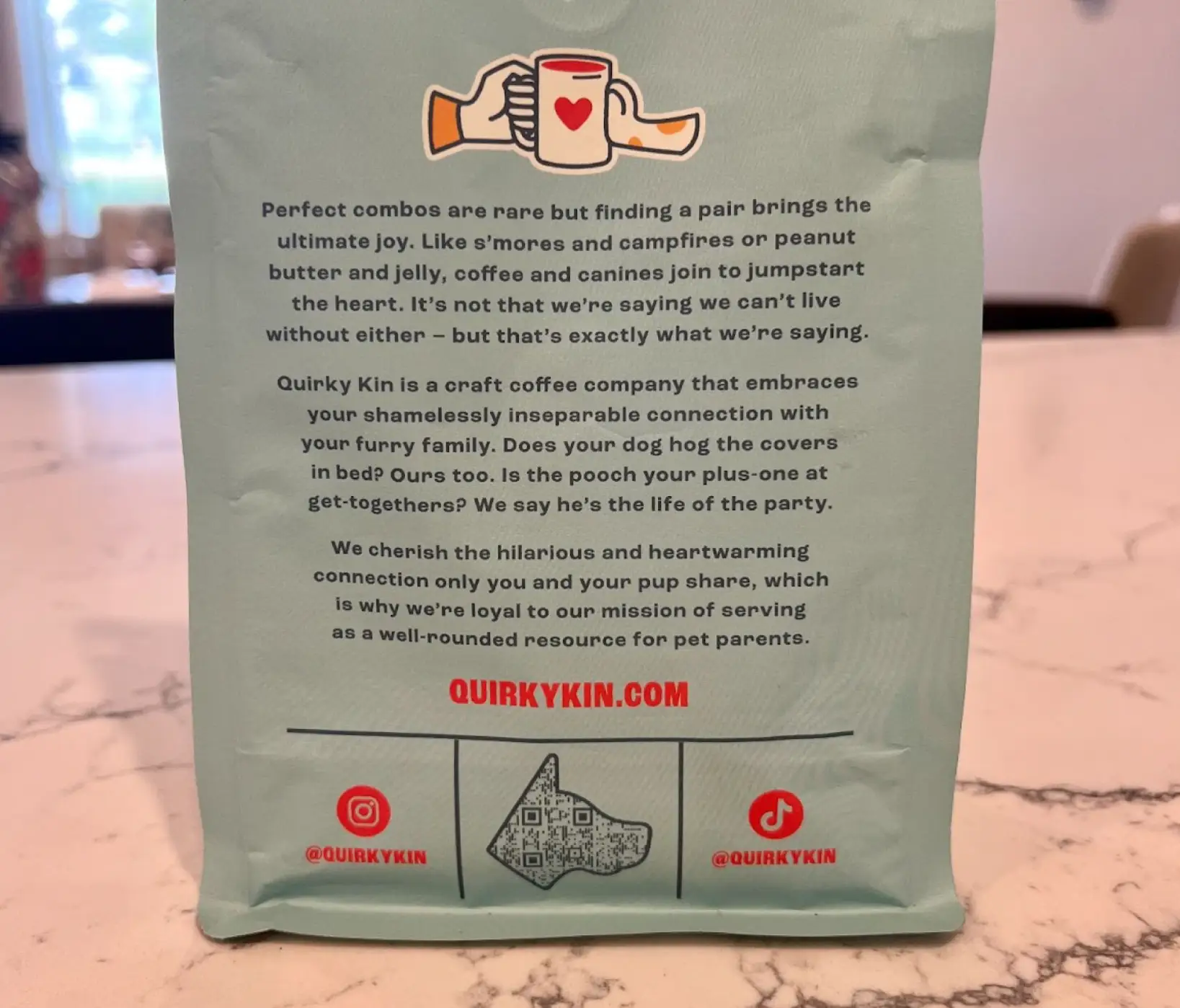 A blue coffee bag with an image of two hands holding a cup and a dog-shaped QR Code at the bottom.