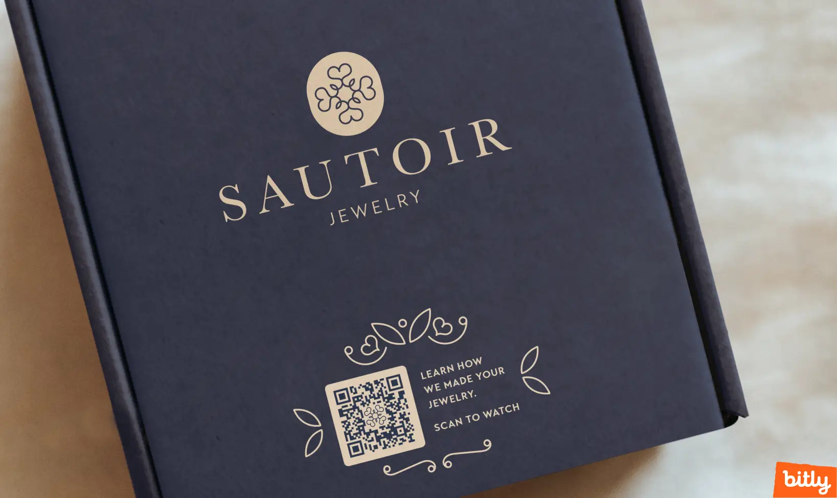 Beige logo, font, and a QR Code against dark blue jewelry packaging.