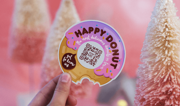 A hand holding a donut-shaped sticker with a QR Code in the middle. 