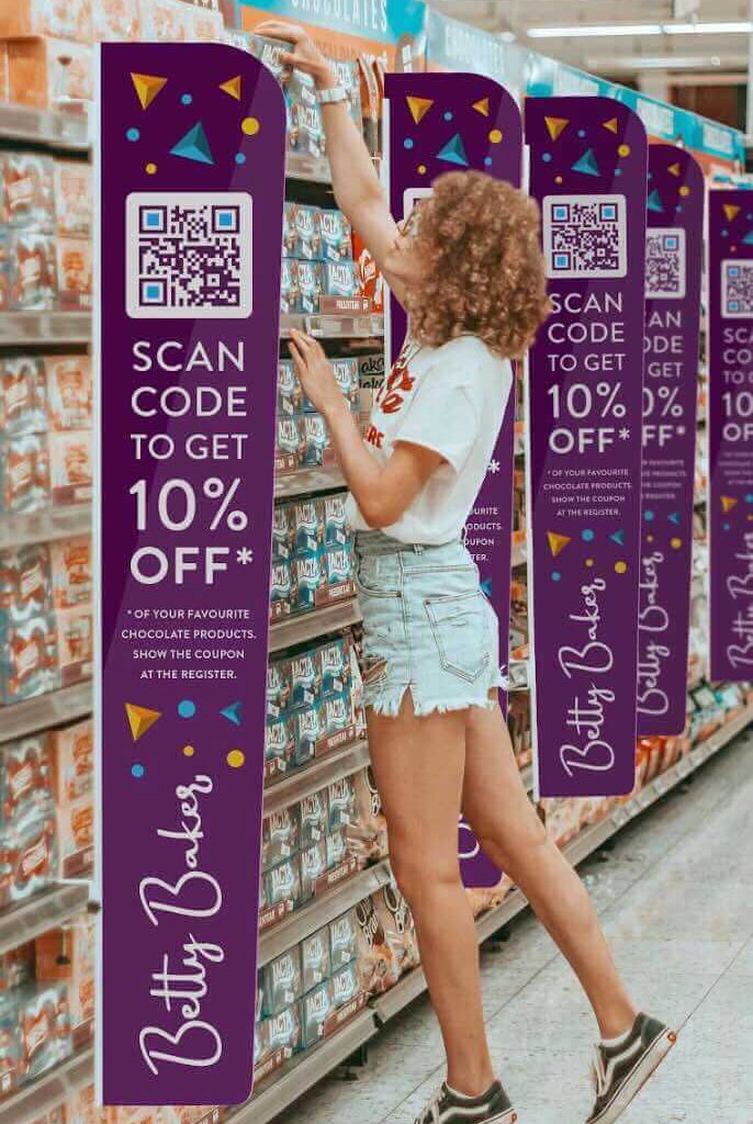 A person in a supermarket reaching for a product on the top shelf with a large scan QR Code to get 10% off banner next to them